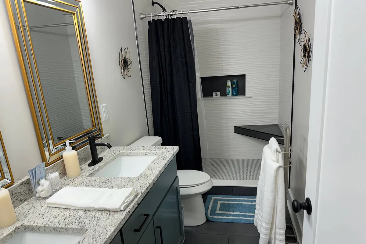 A contemporary bathroom with dual sinks atop a granite countertop, large mirrors, and a modern, glass-enclosed shower area. The fixtures and finishes evoke a sense of luxury and relaxation, making the space ideal for both quick morning routines and unwinding at day's end.