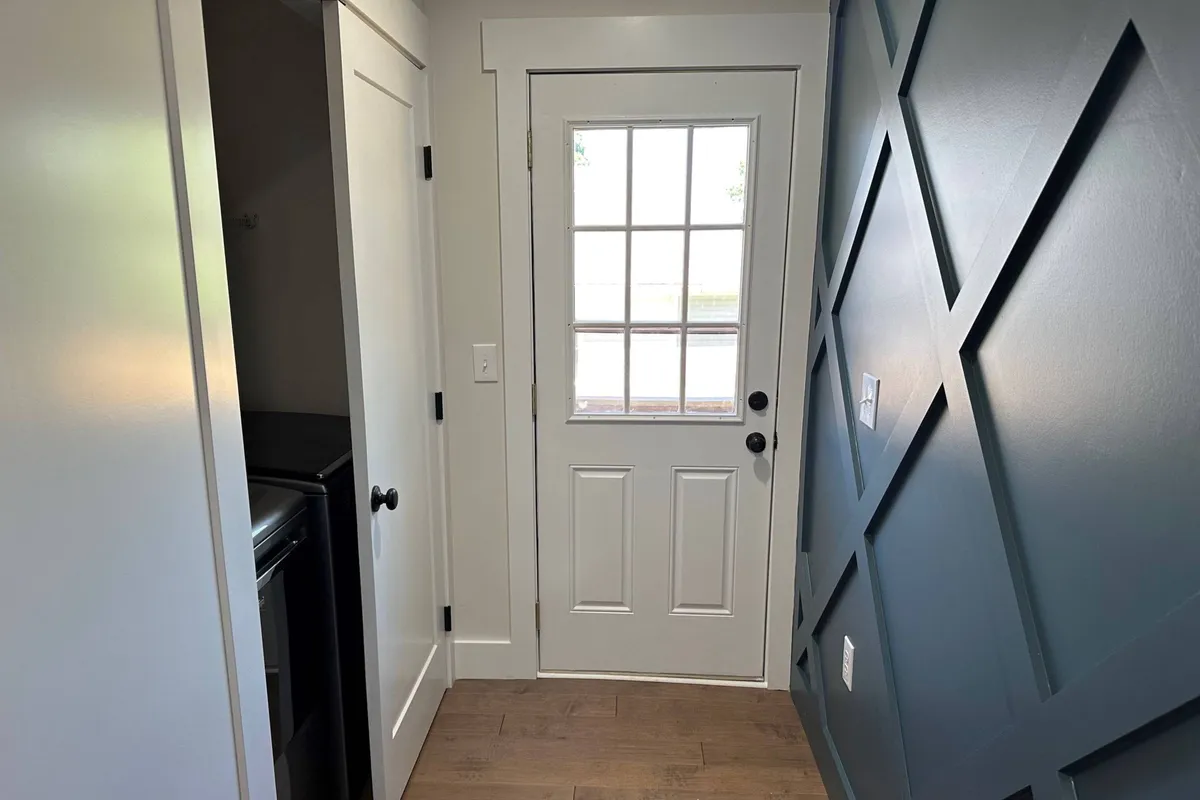 A welcoming entryway featuring the front door, decorative wall paneling, and an open laundry closet. The layout suggests both practicality and a sense of arrival, emphasizing comfort and convenience for extended stays.