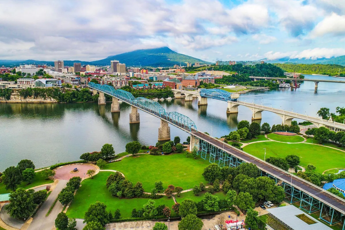 This exterior shot captures a scenic landscape with a river, bridges, city skyline, green parks, and a mountain backdrop. The image is energetic and captures the vibrancy of the area, with visible mountain views enhancing the sense of outdoor escape.
