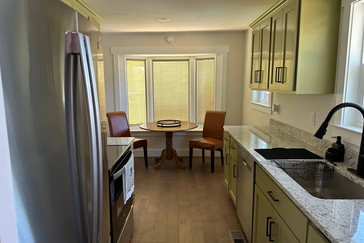 An inviting kitchen and dining area with stainless steel appliances and granite countertops. The round dining table with wooden chairs and a bright bay window creates a cozy spot for sharing meals or sipping coffee. The space balances everyday utility with a welcoming atmosphere for gatherings.