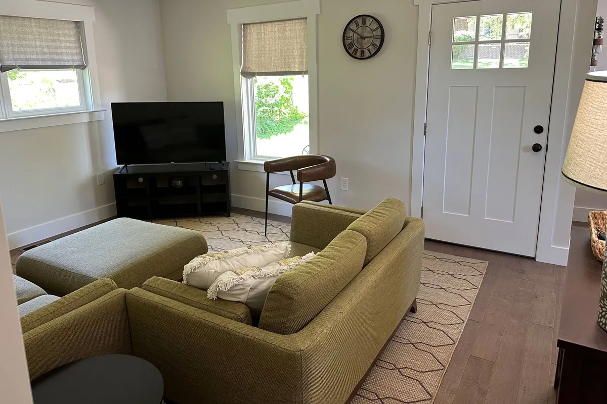 A welcoming living room featuring a green sofa, coffee table, armchair, and a television, all arranged to create a cozy and functional space. Natural light brightens the room through unseen windows, and the open doorway hints at a seamless flow to adjacent areas.